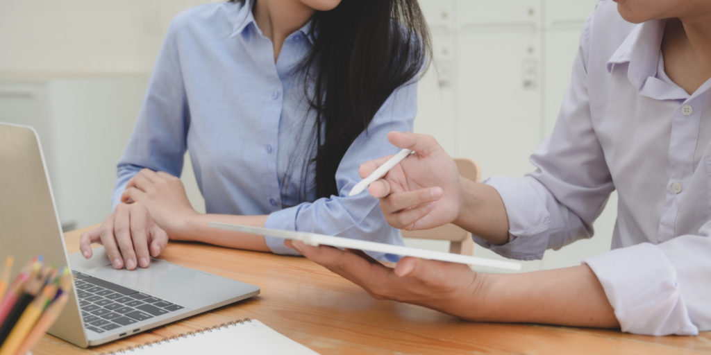 gesturing hands of people at desk next to laptop