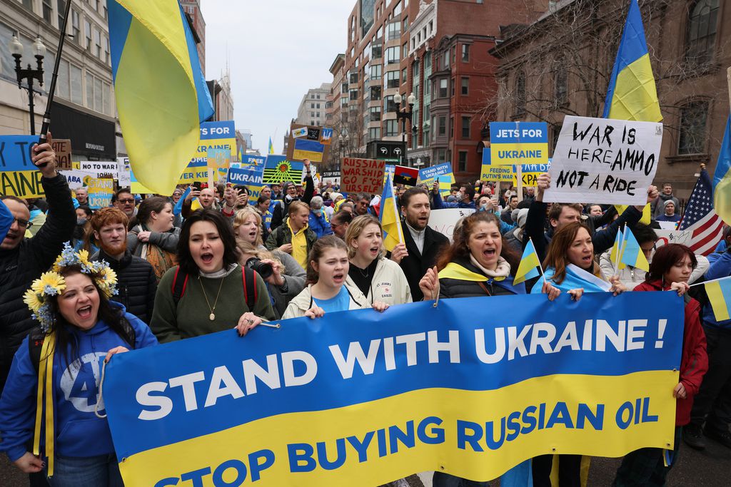 People march down city street carrying yellow and blue signs during a rally in support of Ukraine