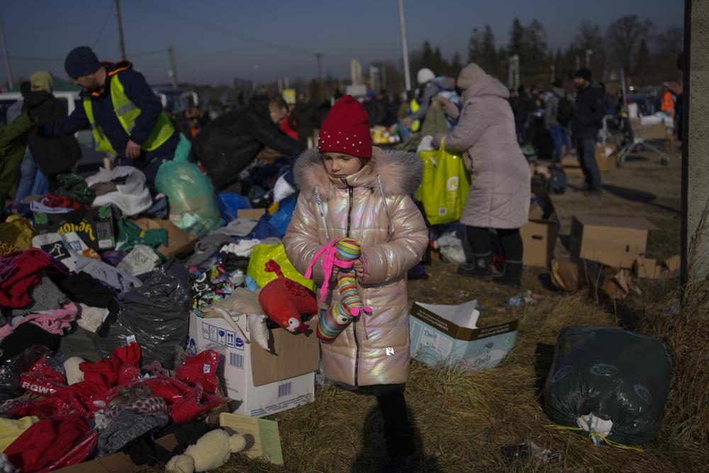 families in winter coats rummage through boxes of donated items in the dark