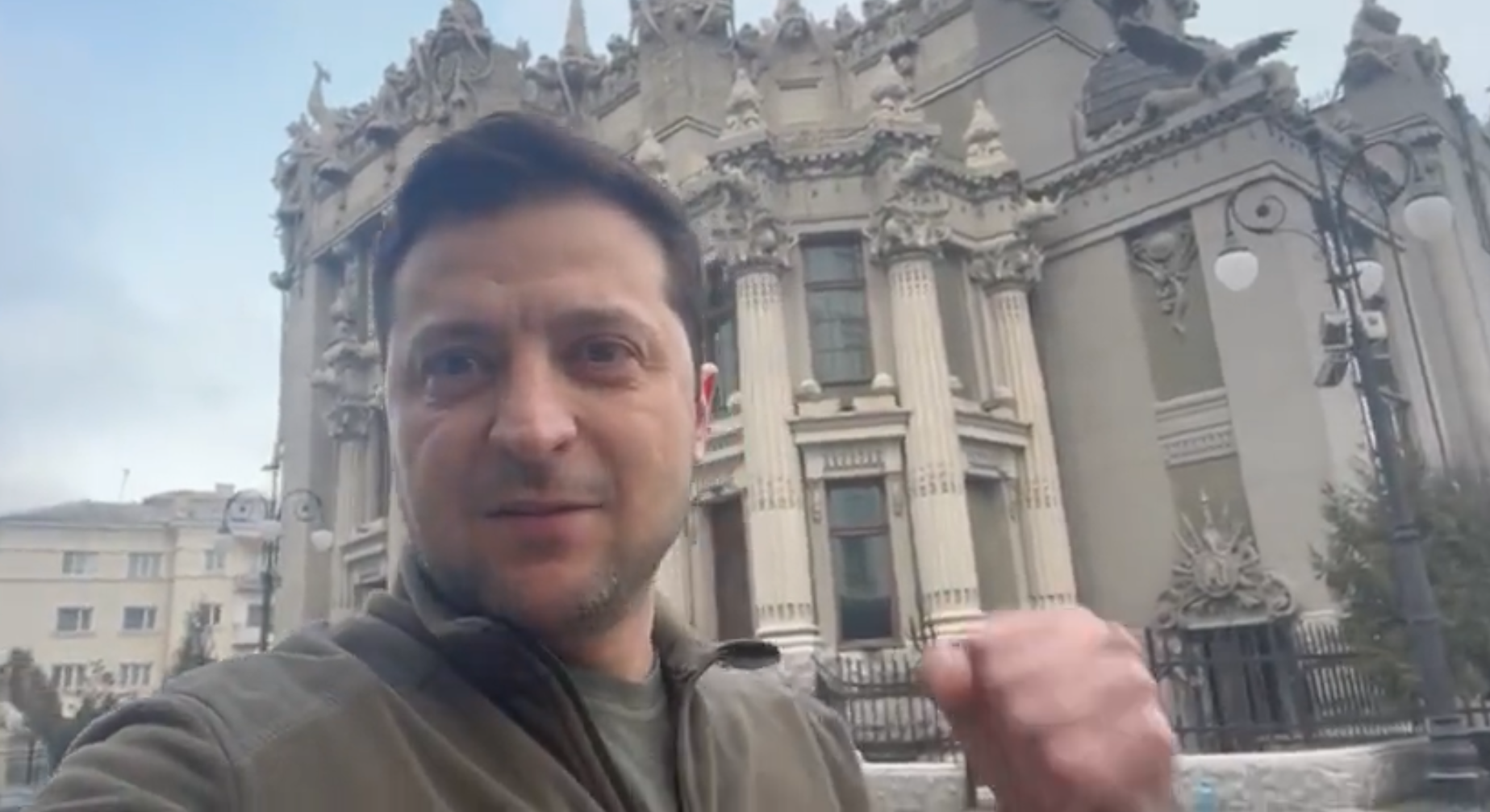 Man with fist raised stands in front of grand building