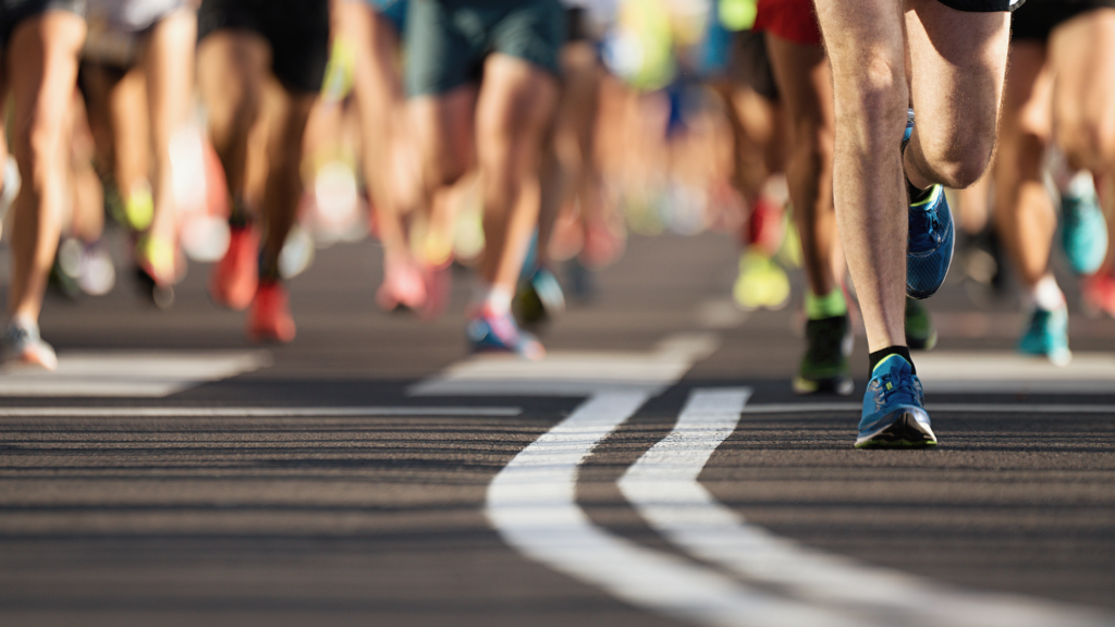 A blog banner that shows the road lines curving, it is blurred in the front of the image and gets more clear further into the image. You can see a bunch of peoples' legs and feet as they are running on the pavement. It is presumed they are running a marathon.